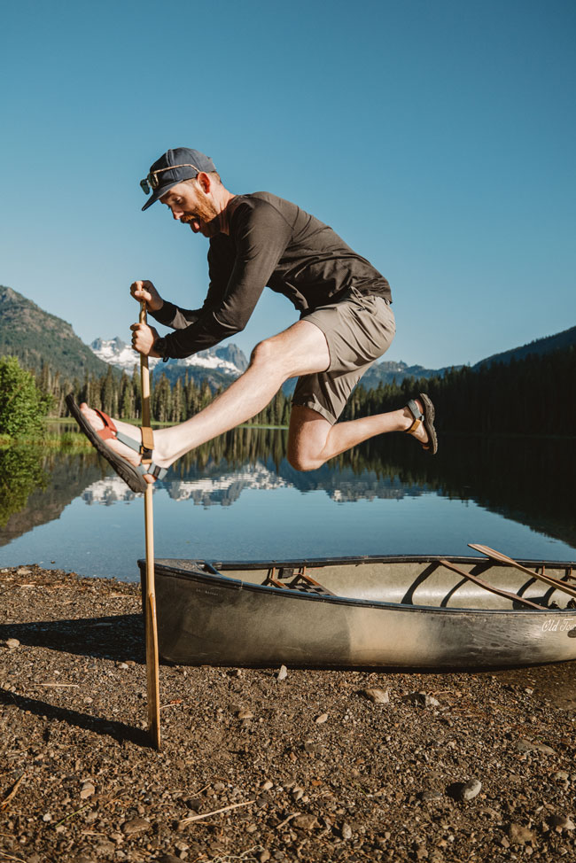 Ben jumps in the air in front of a lake, wearing Hurricane XLT2 sandals.